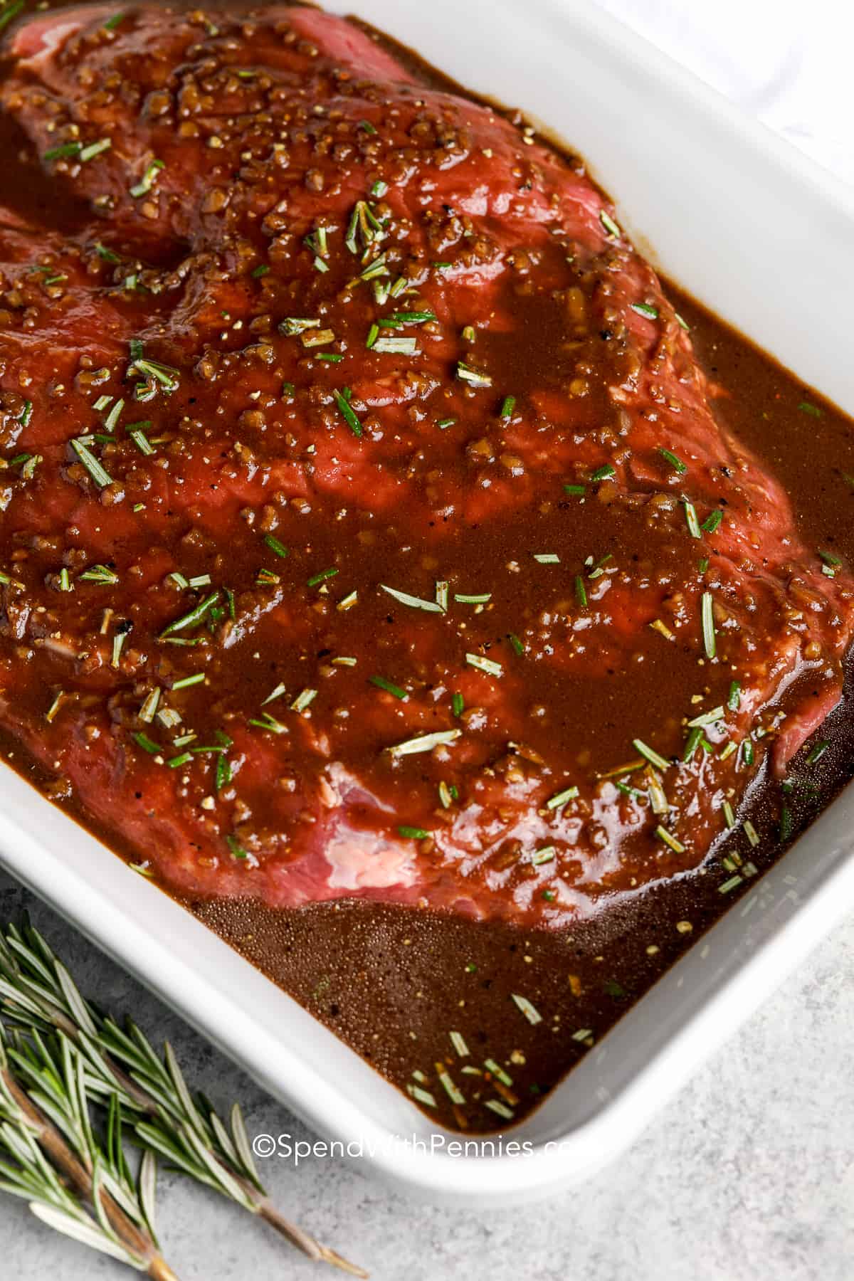 flank steak in marinade in a white baking dish
