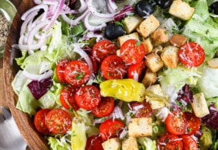 An Italian salad in a wood bowl with dressing and parmesan cheese next to it