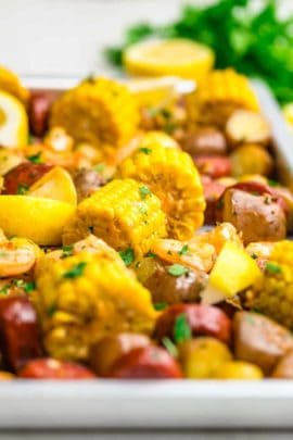 Shrimp boil on a sheet pan with corn, potatoes, shrimp, sausage, parsley, lemon wedges