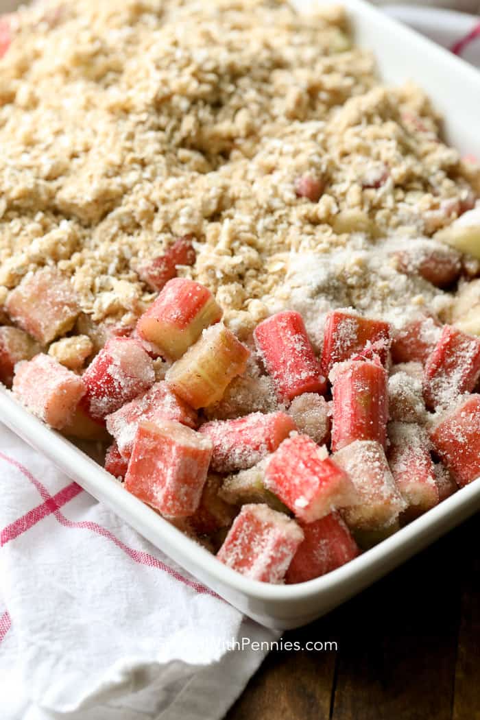 This easy Rhubarb Crisp is a delicious and easy dessert you can make in minutes! With the perfect balance between sweet and tart, rhubarb crisp is family favorite!This easy Rhubarb Crisp is a delicious and easy dessert you can make in minutes! With the perfect balance between sweet and tart, rhubarb crisp is going to be your new summer favorite. #spendwithpennies #easyrecipe #easydessert #rhubarbcrisp #strawberryrhubarb #withoatmeal #bakedrecipe #fruitcrisp Rhubarb Crisp being prepared in a white baking dish