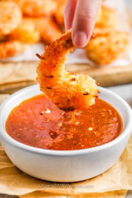 A breaded shrimp being dipped in a bowl of sweet chili sauce